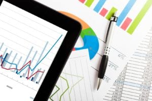 iPad and pen on top of papers with various charts and graphs